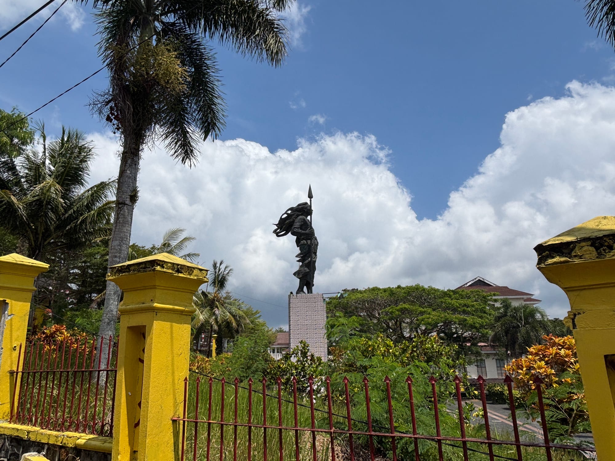 The Martha Christina Tiahahu monument, a statue holding a spear, seen through a yellow gate