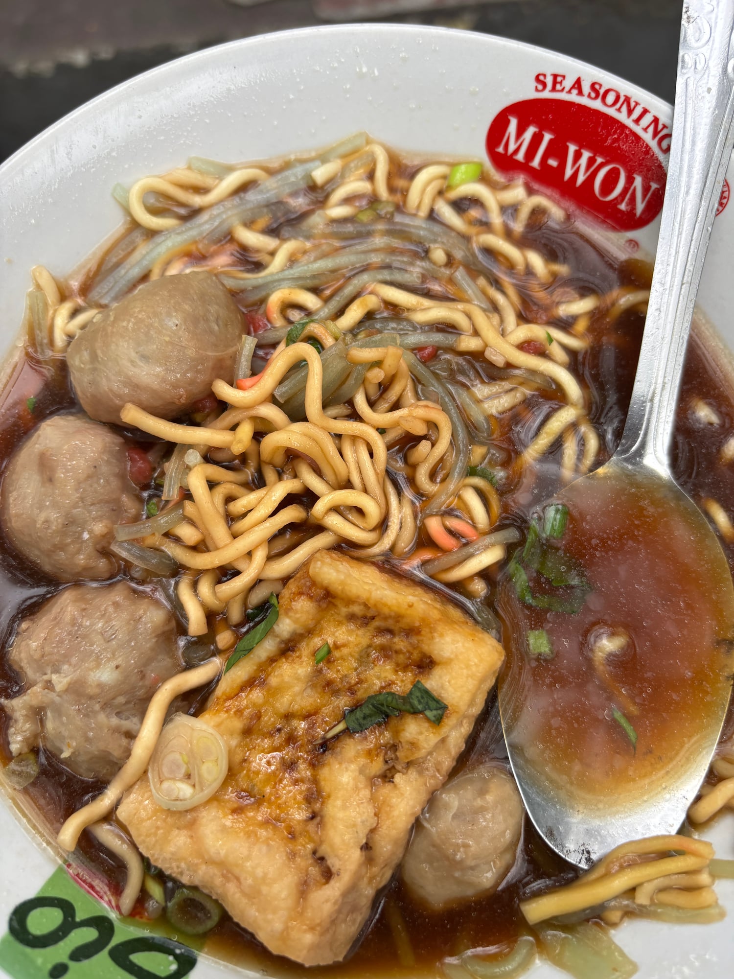 A bowl of Bakso meatball soup with noodles, tofu, and meatballs