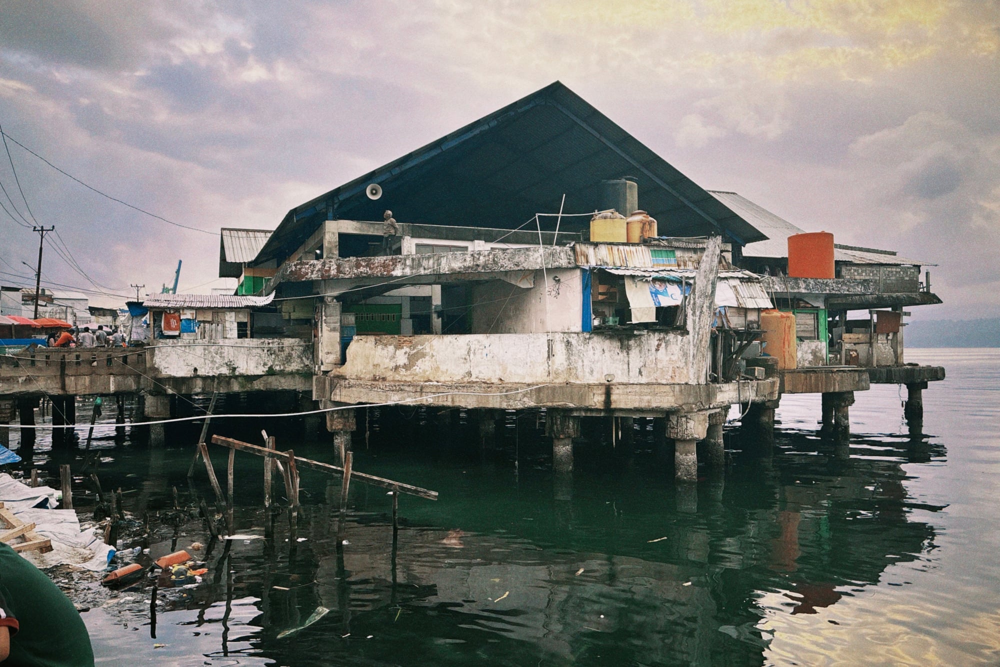 A weathered building on stilts over polluted water near the Ambon fish market