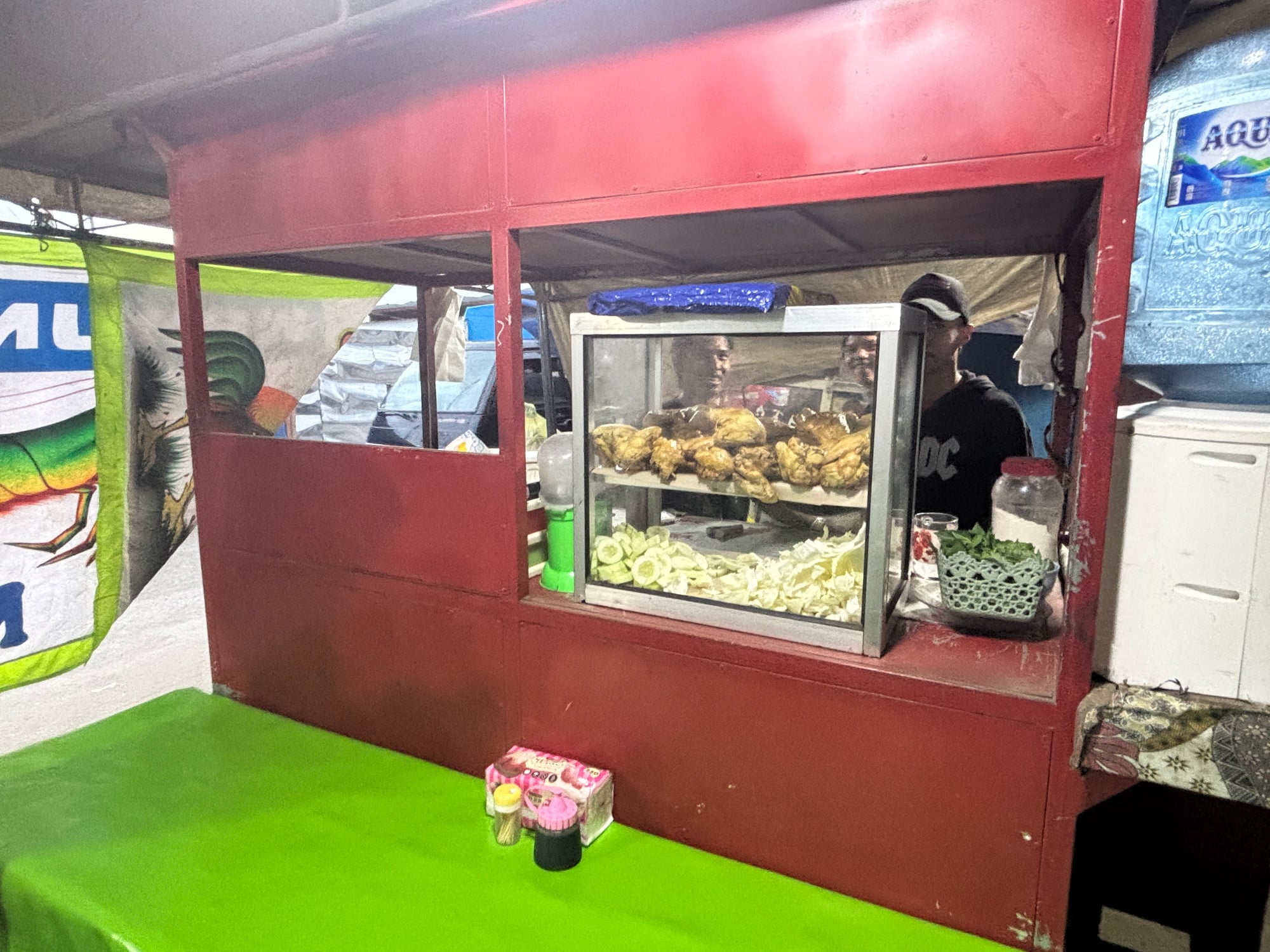 A small food stall with a display case of fried chicken and fresh vegetables