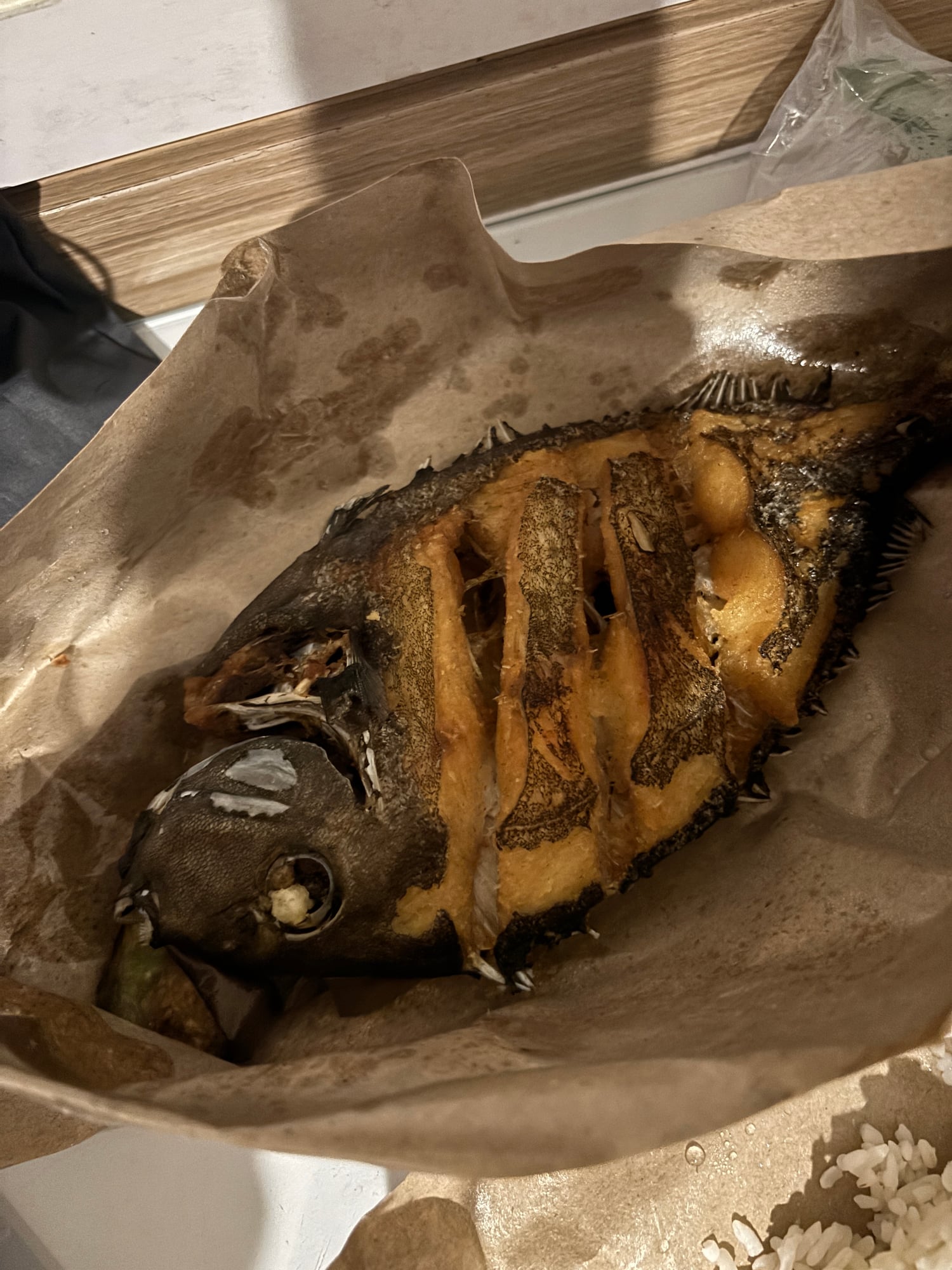A whole fried fish served in a paper takeout box with rice