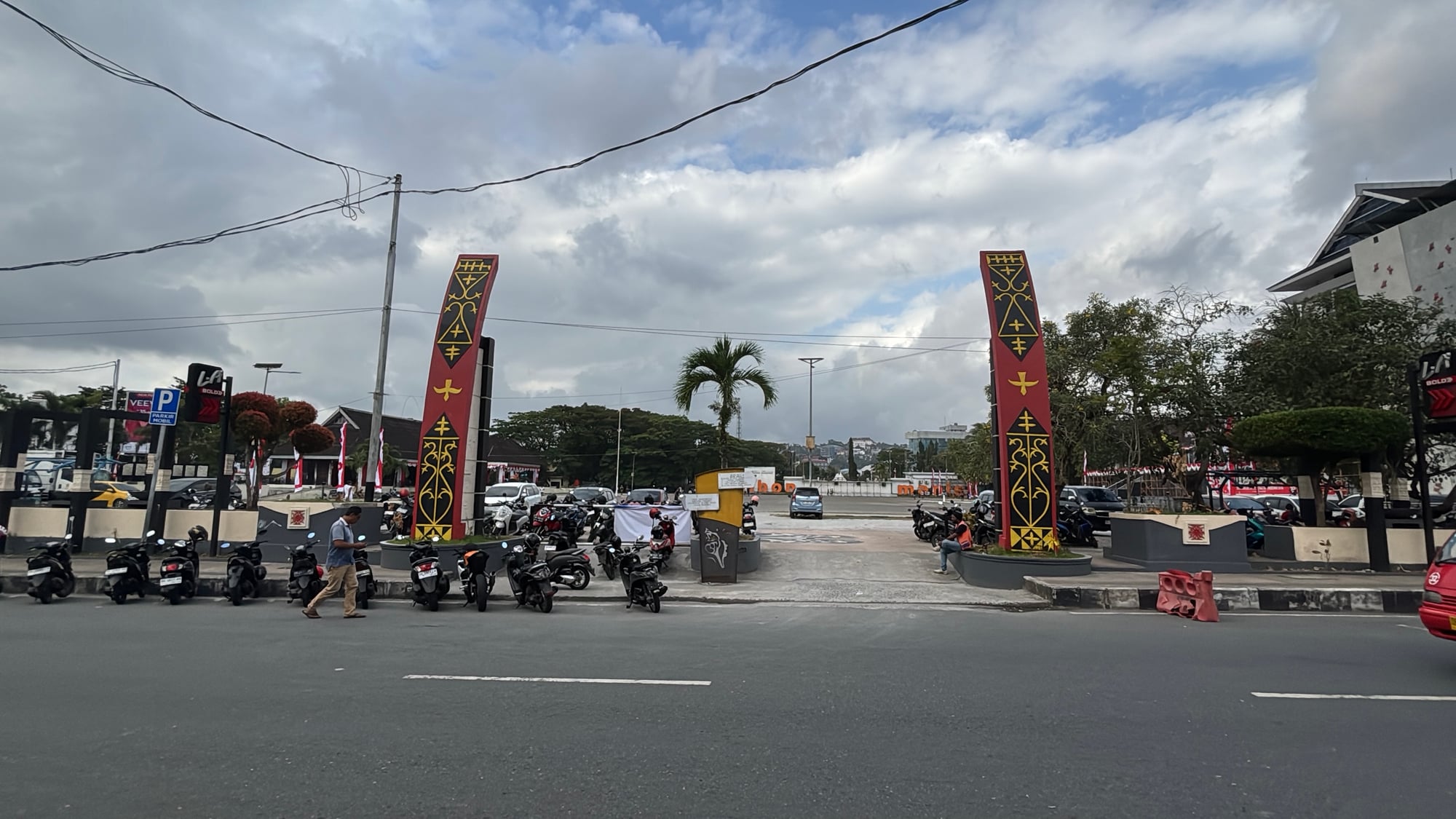 Tall red, black, and gold monuments carved with Timor cultural motifs along a city street