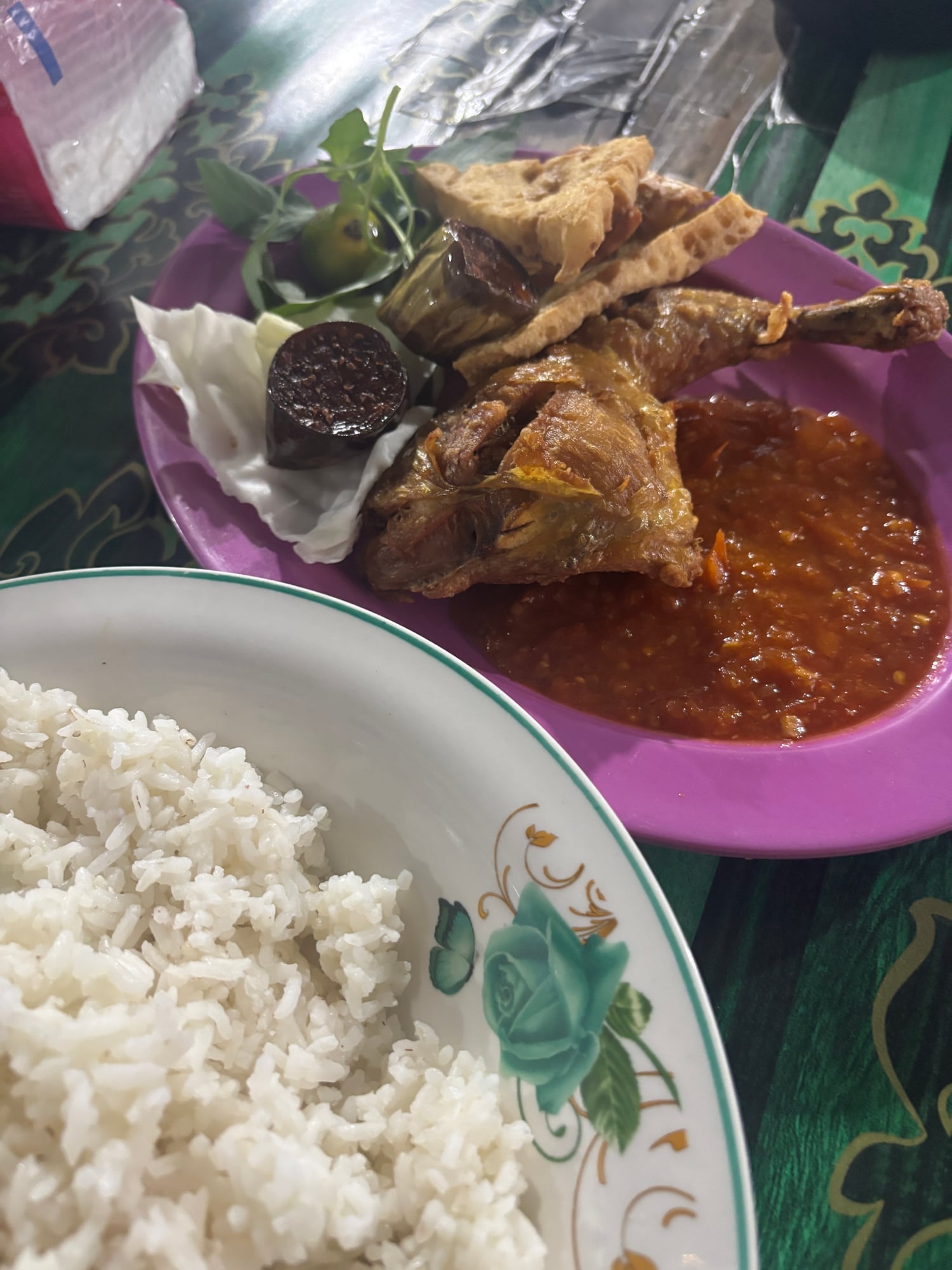 A plate of Nasi Geprek smashed fried chicken with sambal and a bowl of rice