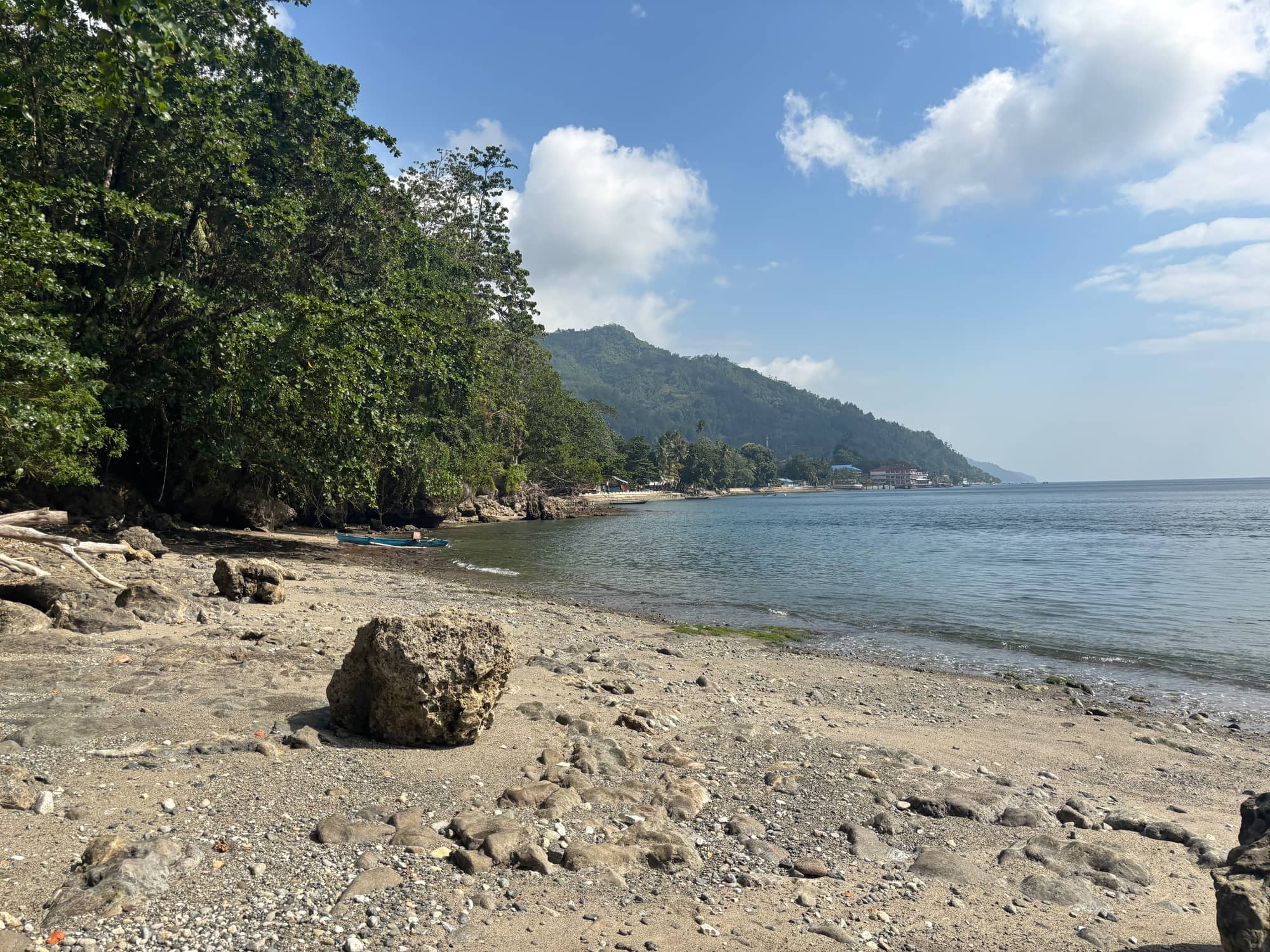 A quiet, empty beach with a small boat and hills in the distance
