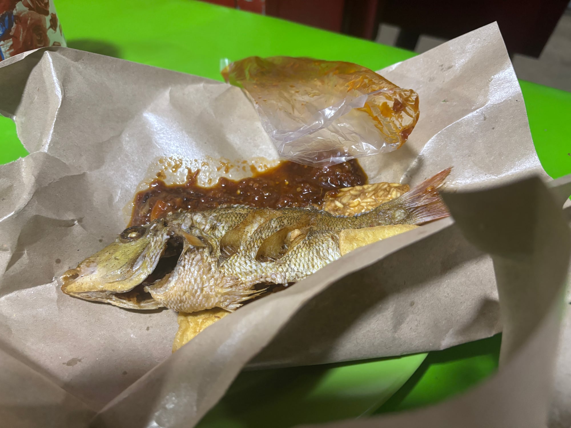 A whole fried fish served with sambal, wrapped in paper
