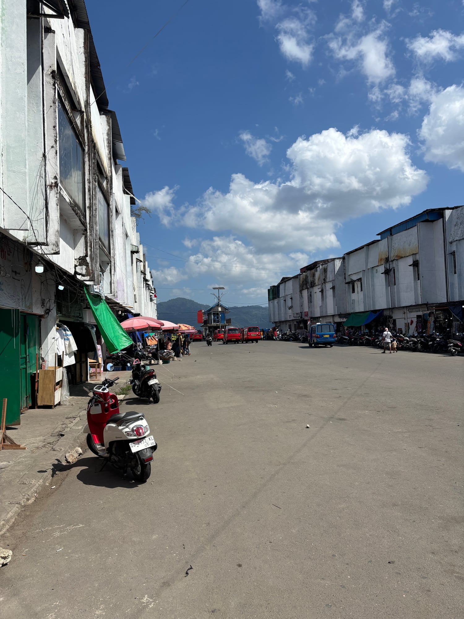 A busy market street near the port with motorbikes and mountains in the background