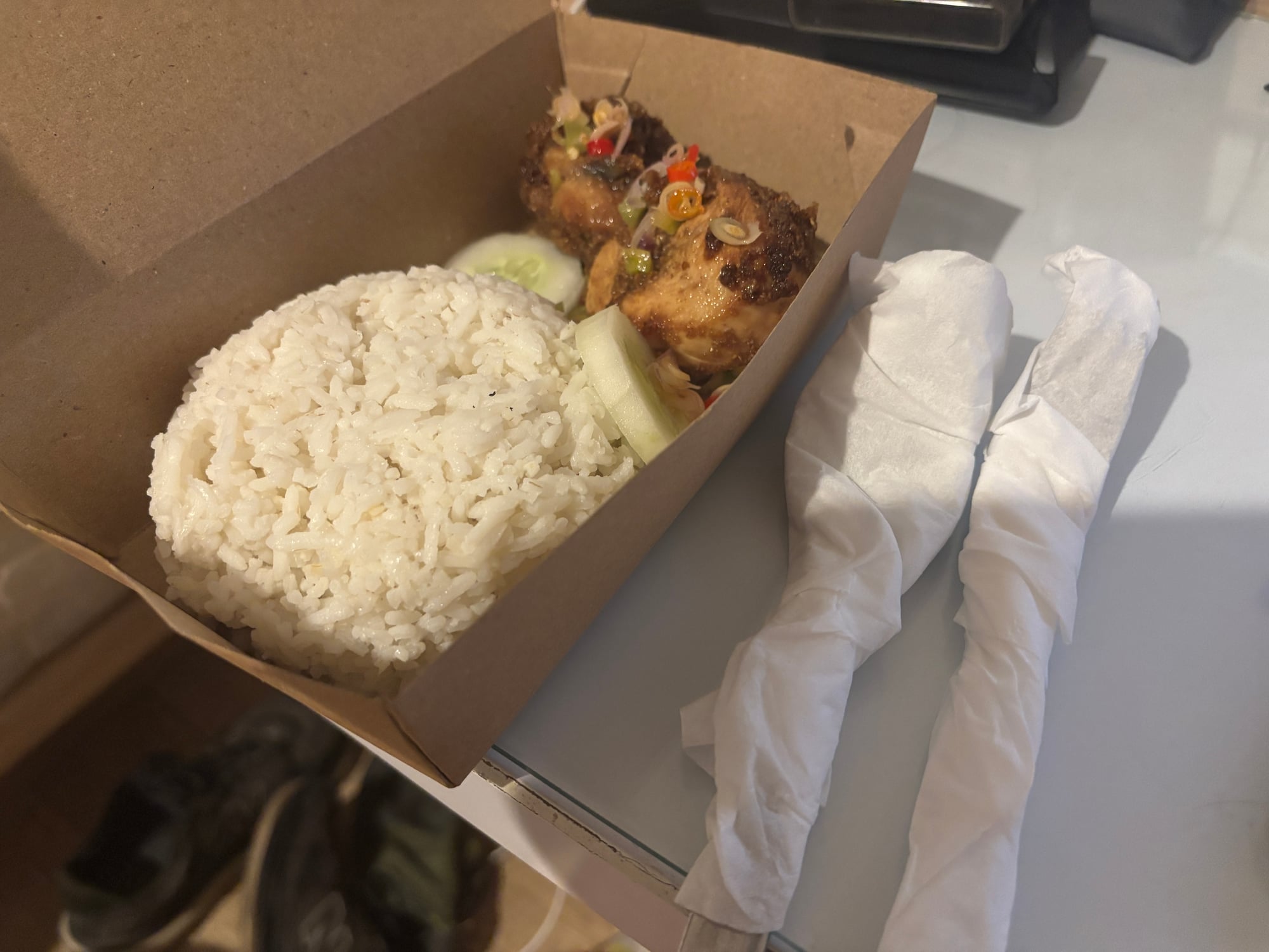 A takeaway box of Nasi Ayam, rice and fried chicken with cucumber