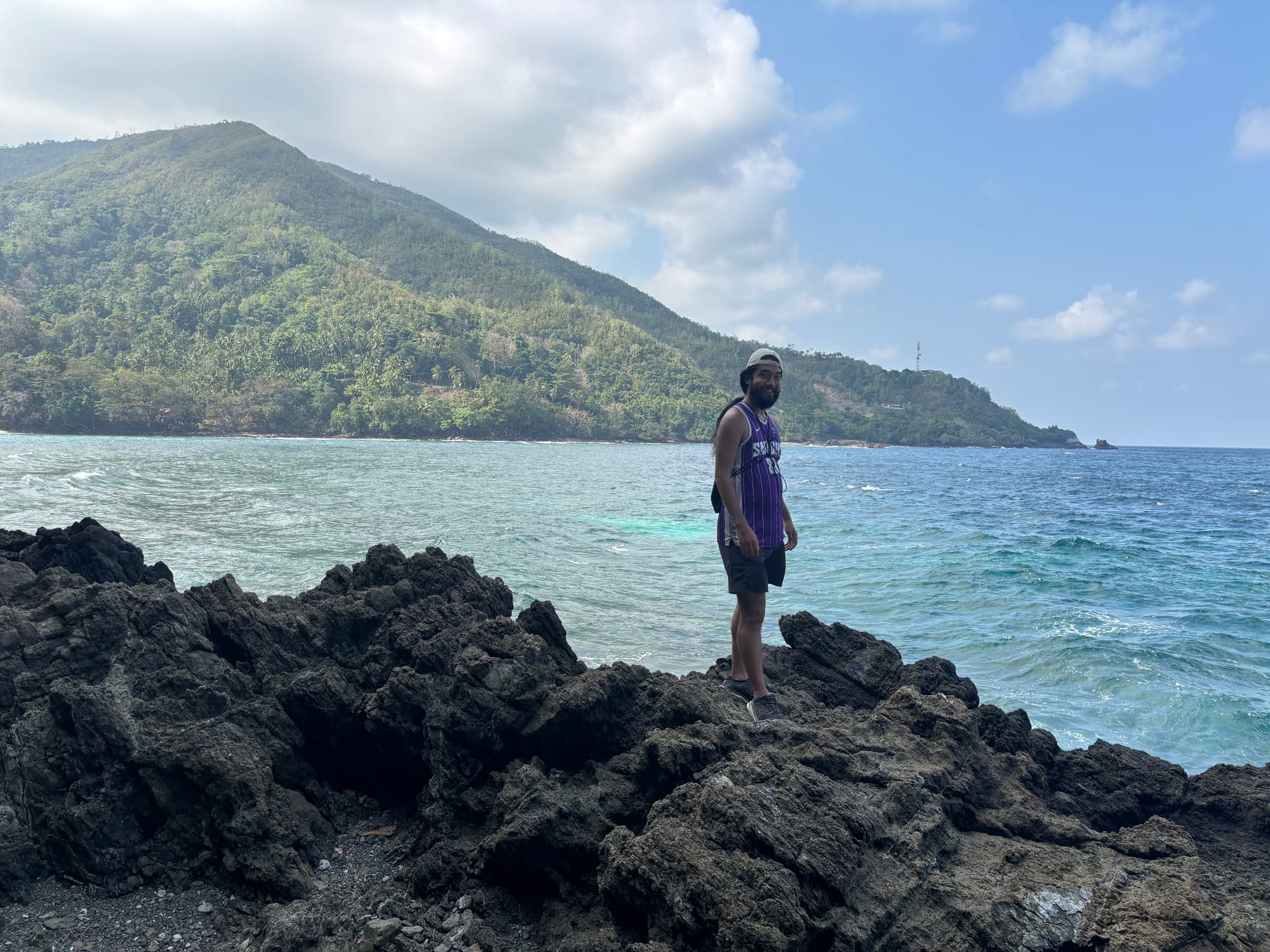 Standing on volcanic rocks overlooking a hidden ocean bay near Ambon