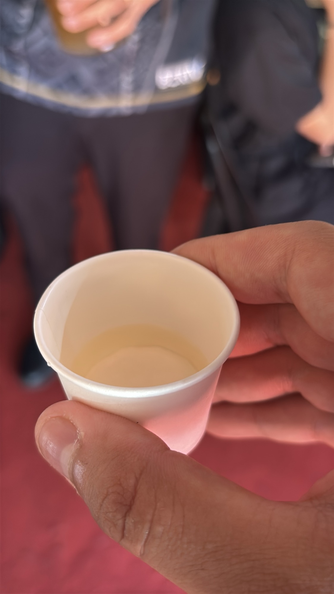 Holding a small paper cup of traditional rice wine for a taste test