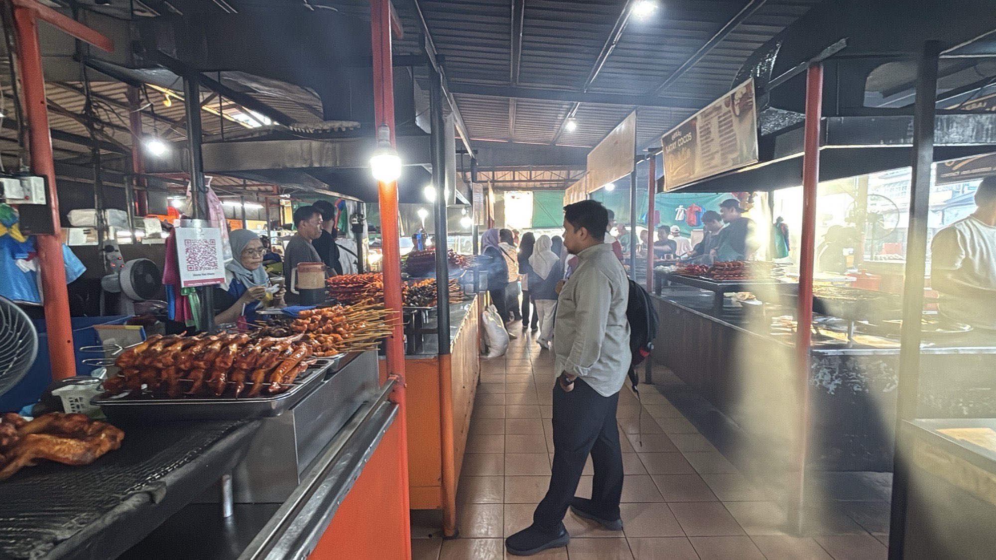 Walking past a row of satay stalls inside a covered market