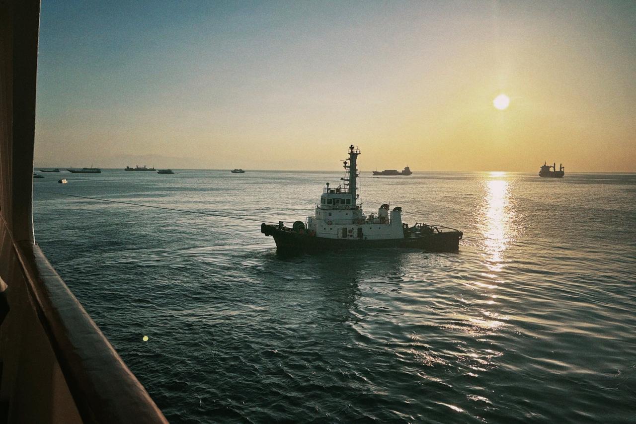 Sebuah kapal tunda bermanuver di dekat feri saat matahari terbit selama persinggahan