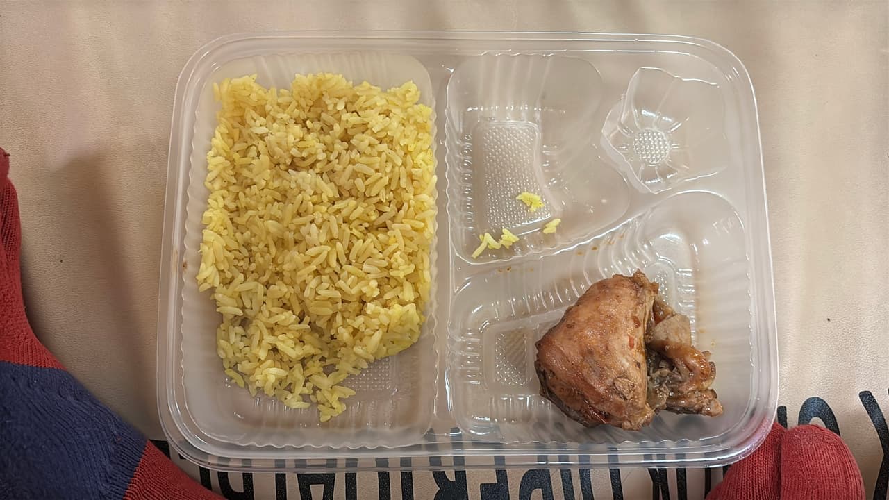 Nampan sarapan feri berisi nasi dan sepotong kecil daging, dengan sebagian besar sekat yang kosong