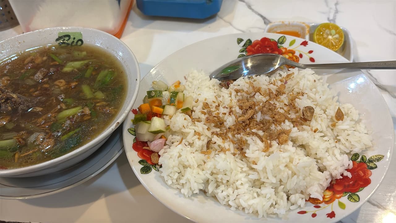 A bowl of Sop Iga beef rib soup next to a plate of rice with fried shallots