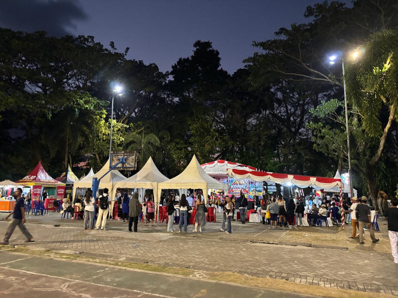 A crowd gathered under tents at a nighttime outdoor event in the park