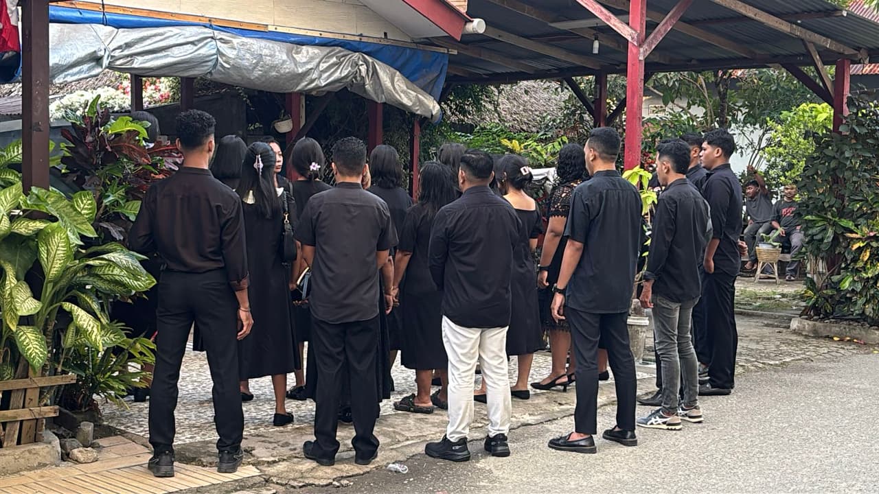 A group of about 20 people dressed in black practicing a cappella singing on an Ambon street