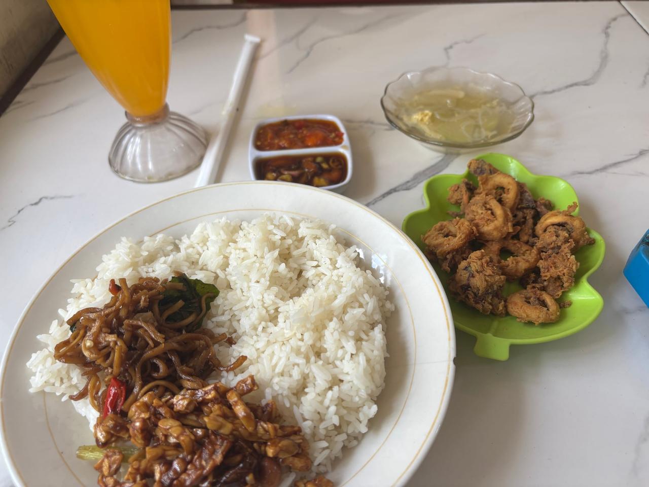 A plate of fried Cumi-cumi (squid), rice, noodles, sambal, and orange juice