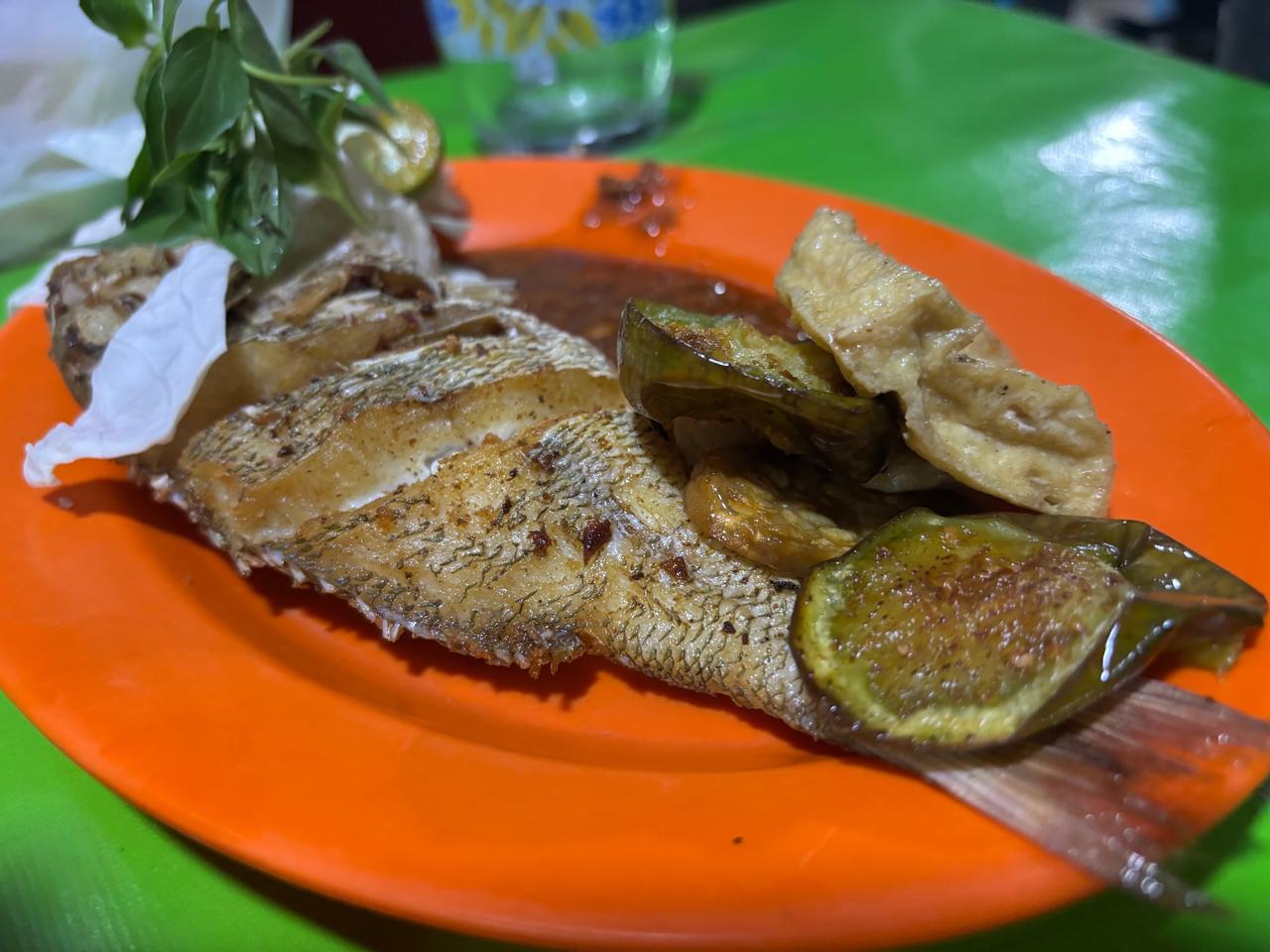 A whole fried fish served with lime and vegetables on an orange plate