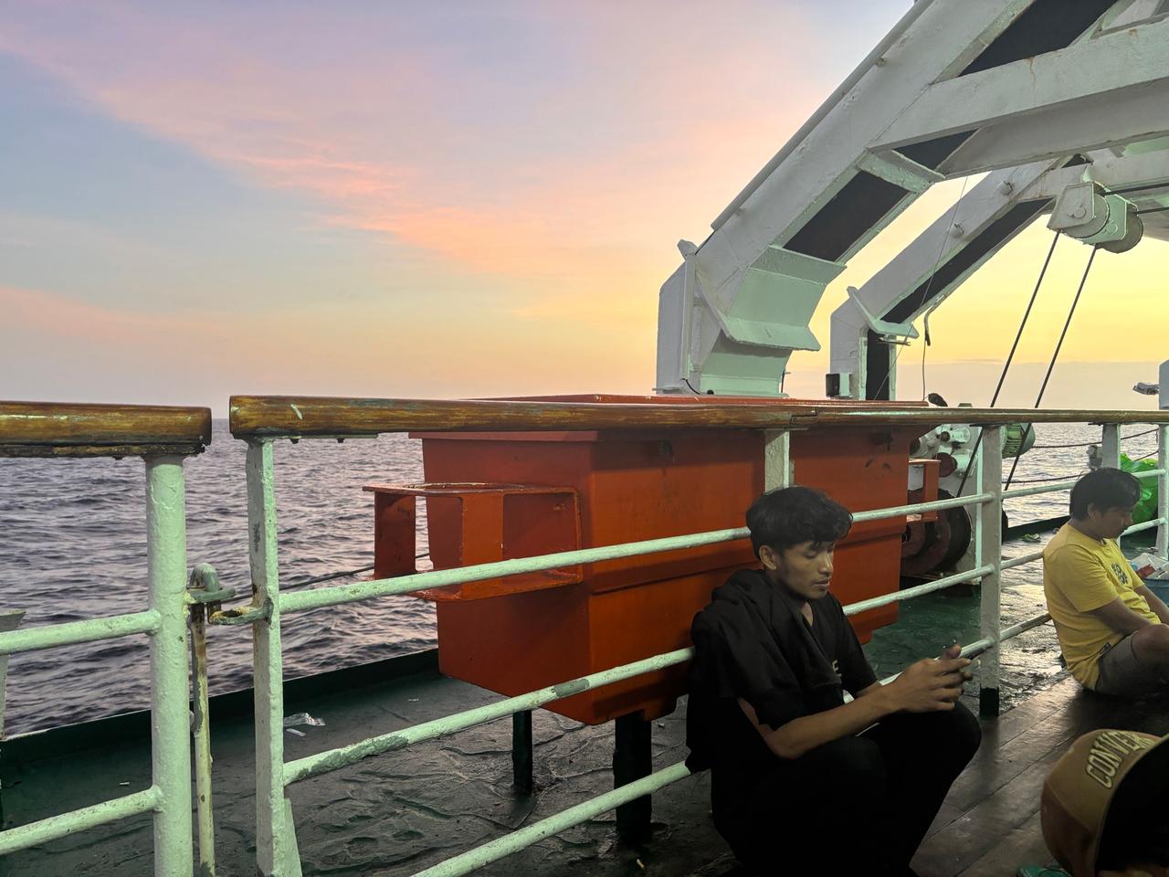 Penumpang bersantai di geladak luar saat senja dalam perjalanan feri