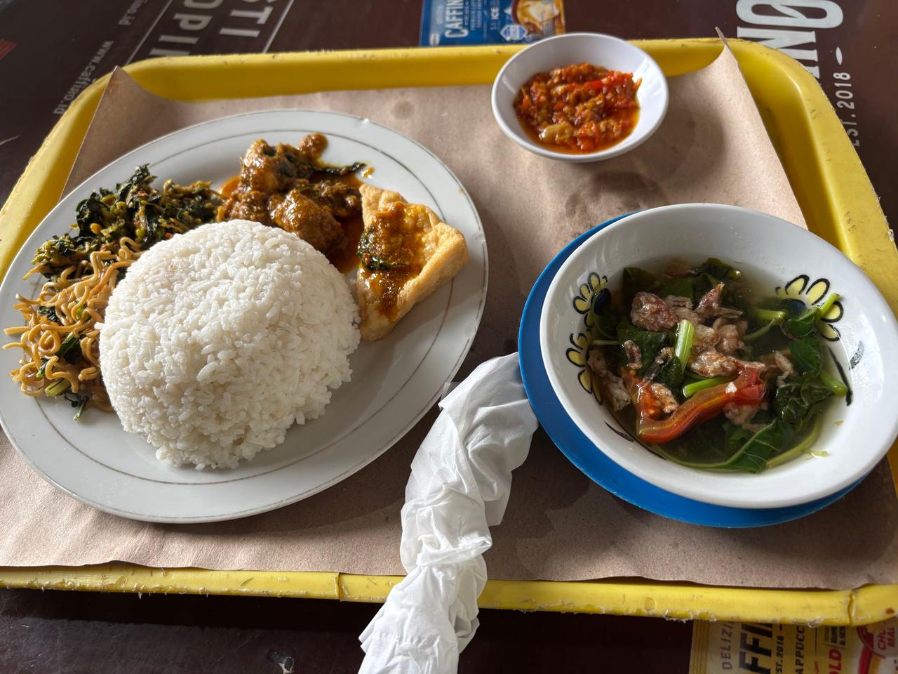 A breakfast tray with soup, tahu, ayam, rice, and crispy mi goreng from a local food stand