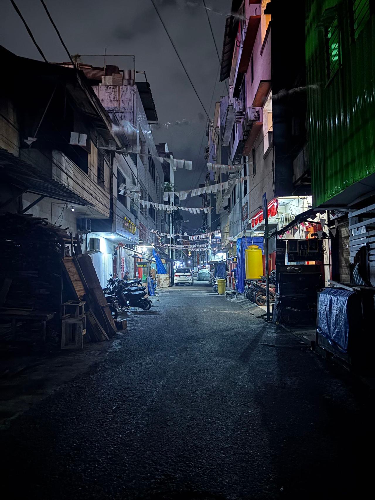 A quiet, narrow back alley lit by scattered lights at night