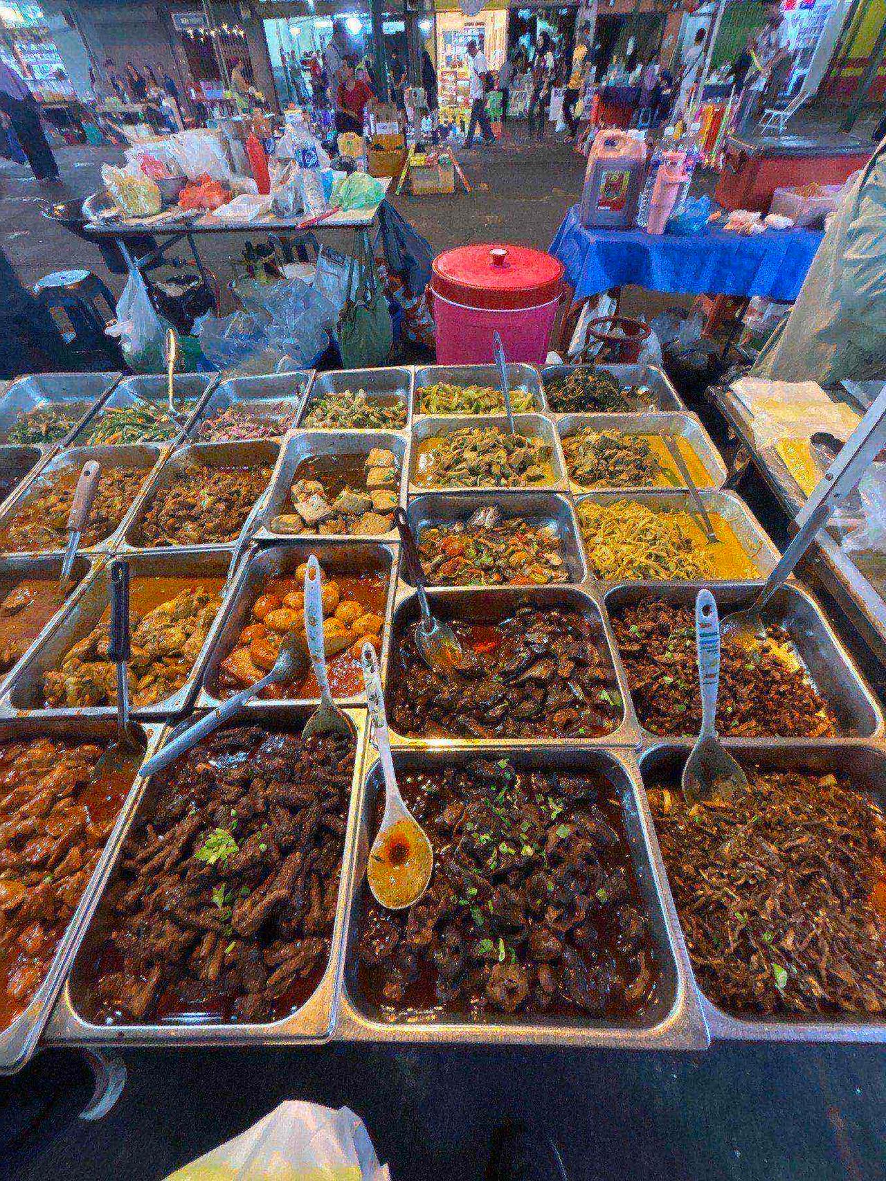 Trays of assorted cooked dishes laid out at a food stall