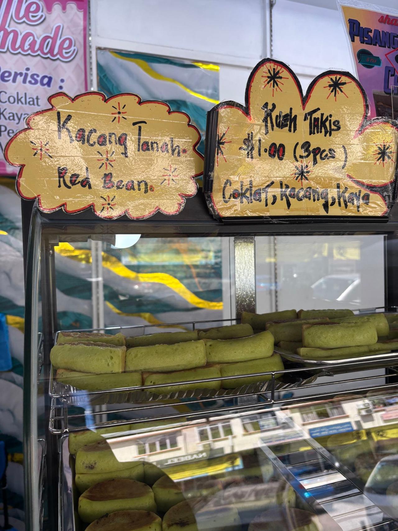 A handwritten sign advertising "Kueh Takis" with chocolate, peanut, and kaya fillings
