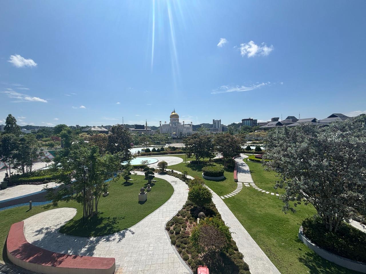 A wide view over a manicured park with the Omar Ali Saifuddien Mosque's golden dome in the distance