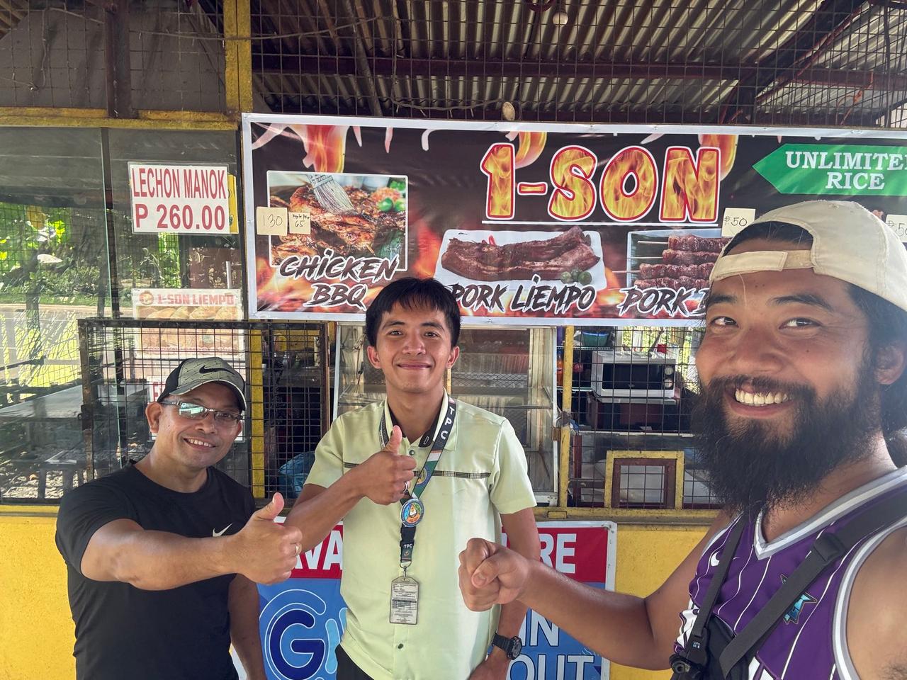 Posing with a university student and a local shop owner at a chicken BBQ stand