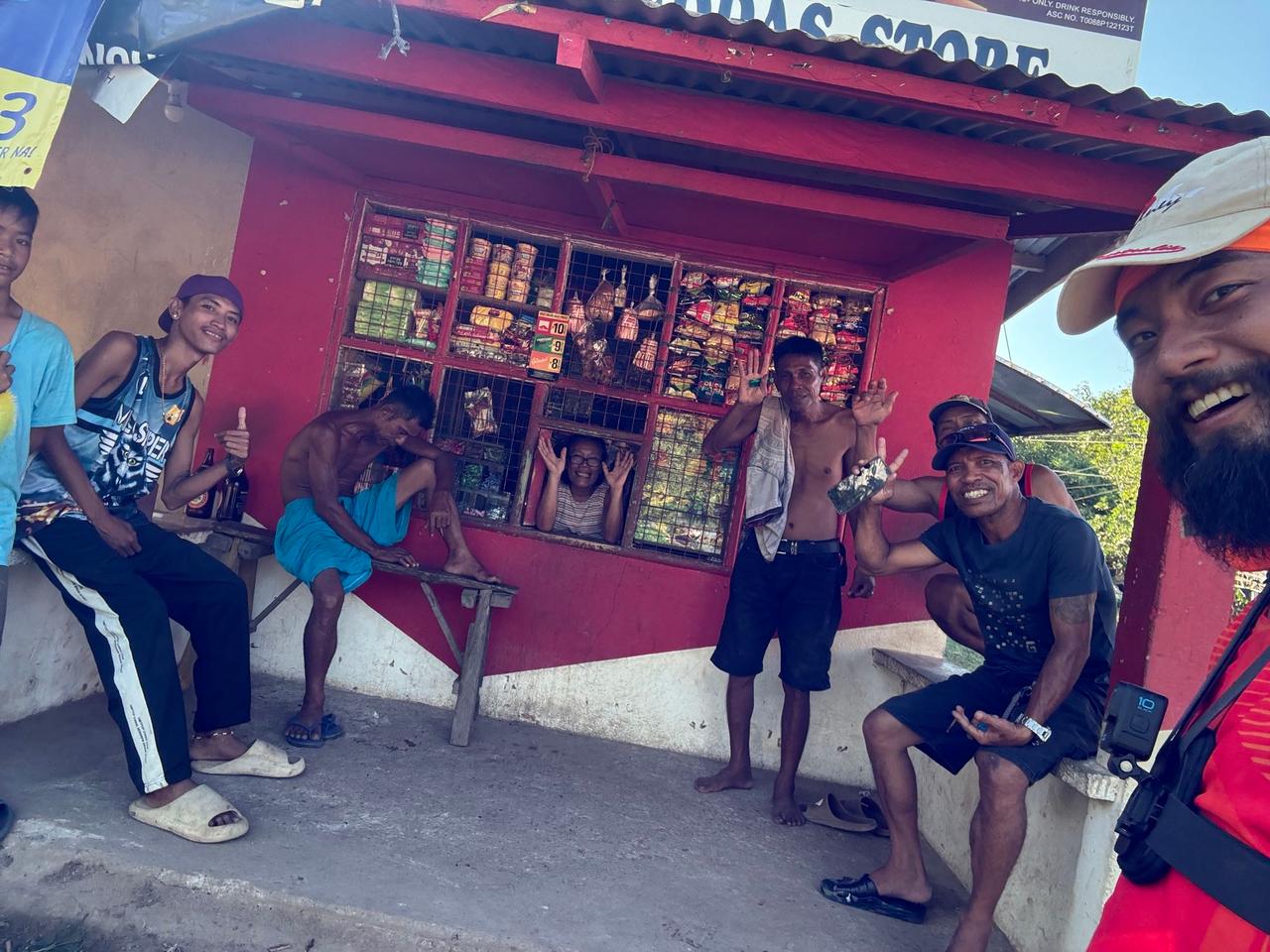 A group of locals gathered and waving in front of a small red sari-sari store