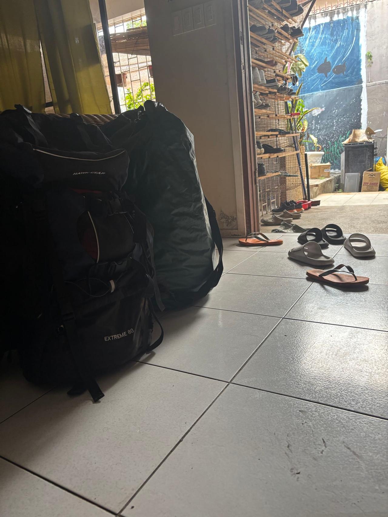A packed travel backpack and duffel bag by the doorway of a guesthouse