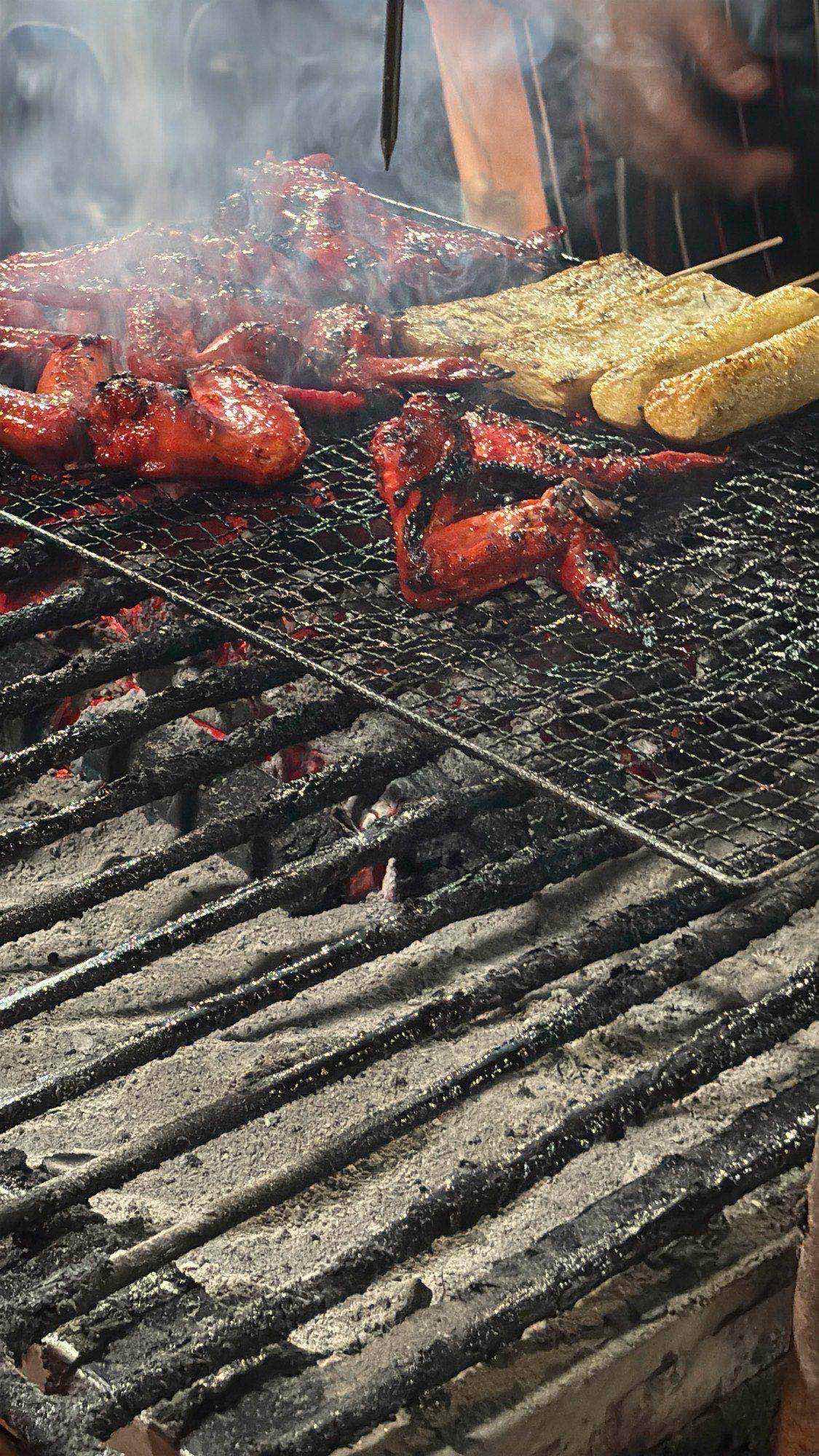 Chicken wings and fish cake sizzling over a charcoal grill