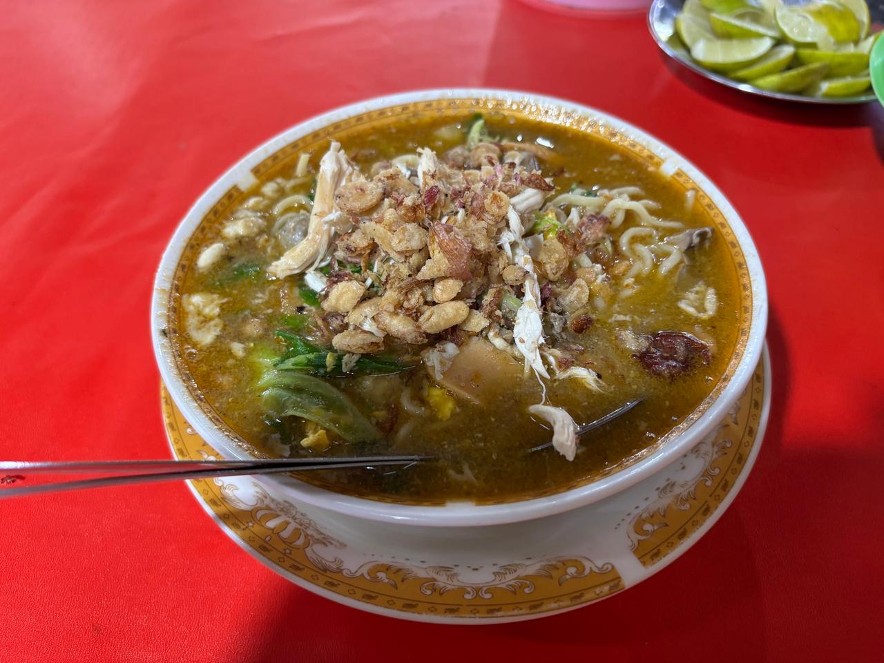 Semangkuk Mie Kuah dengan taburan ayam suwir, bawang goreng, dan kacang tanah, disajikan dengan irisan jeruk nipis