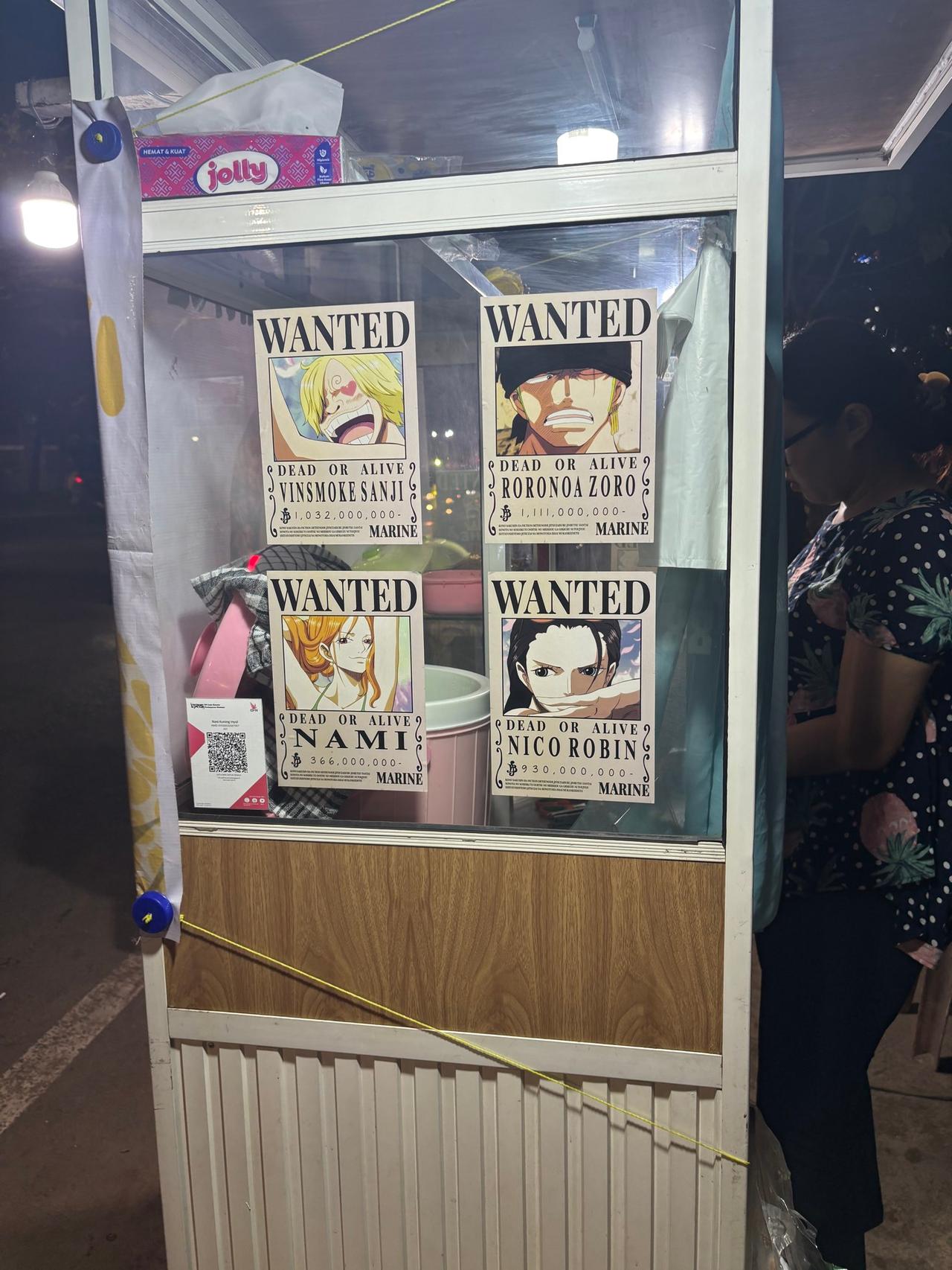 Sebuah etalase di lapak pasar malam yang dipenuhi poster WANTED anime One Piece