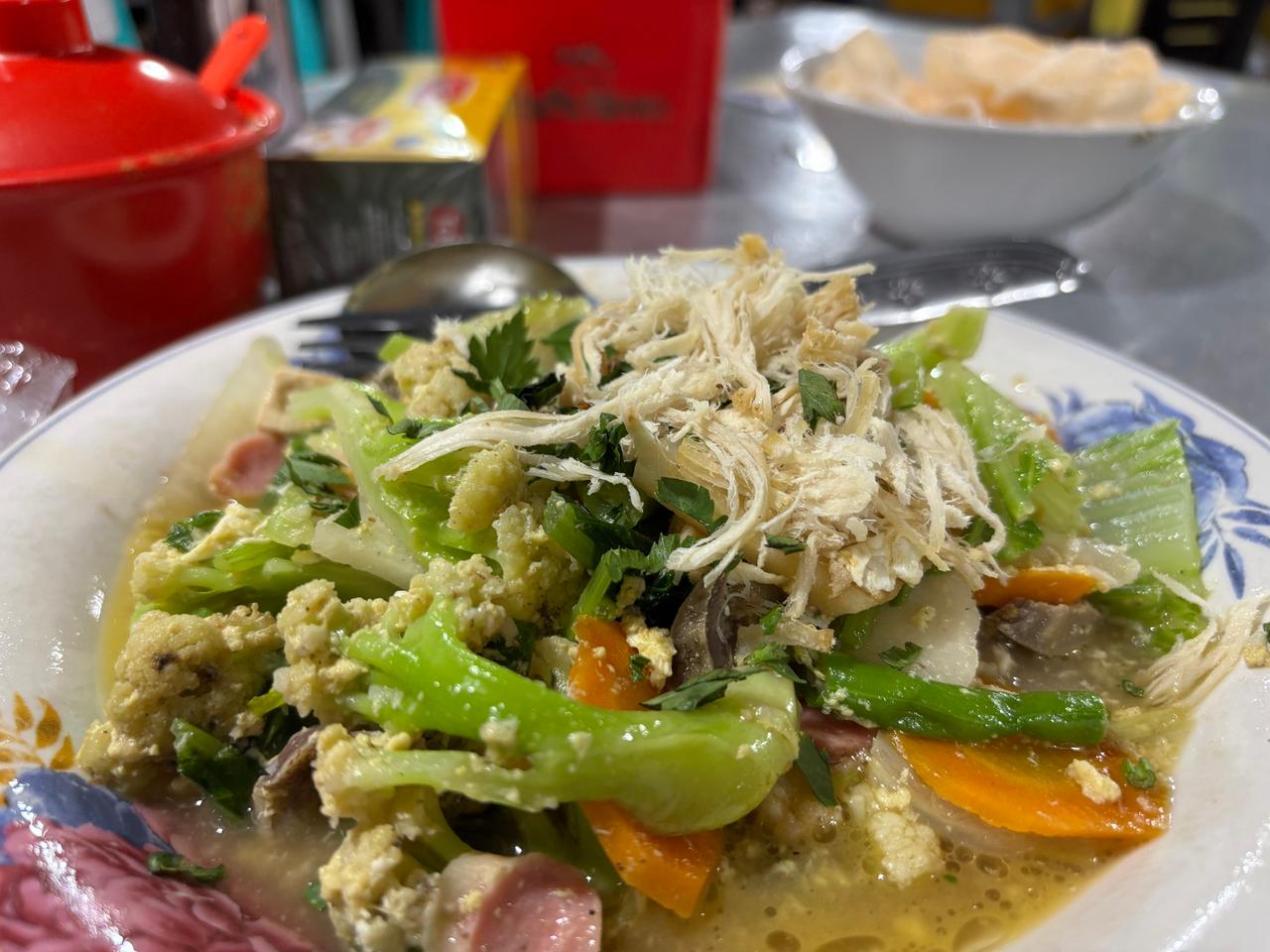 A plate of stir-fried vegetables with egg, carrot and shredded chicken on top