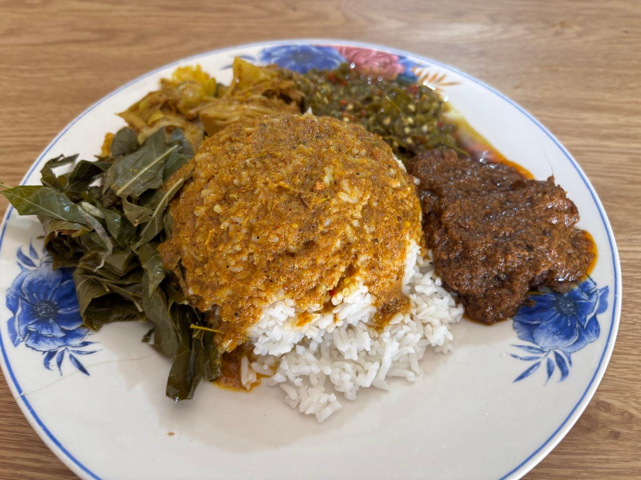 Sepiring Nasi Rendang dengan nasi, rendang daging sapi berbumbu, daun singkong, dan sambal di sebuah warung lokal