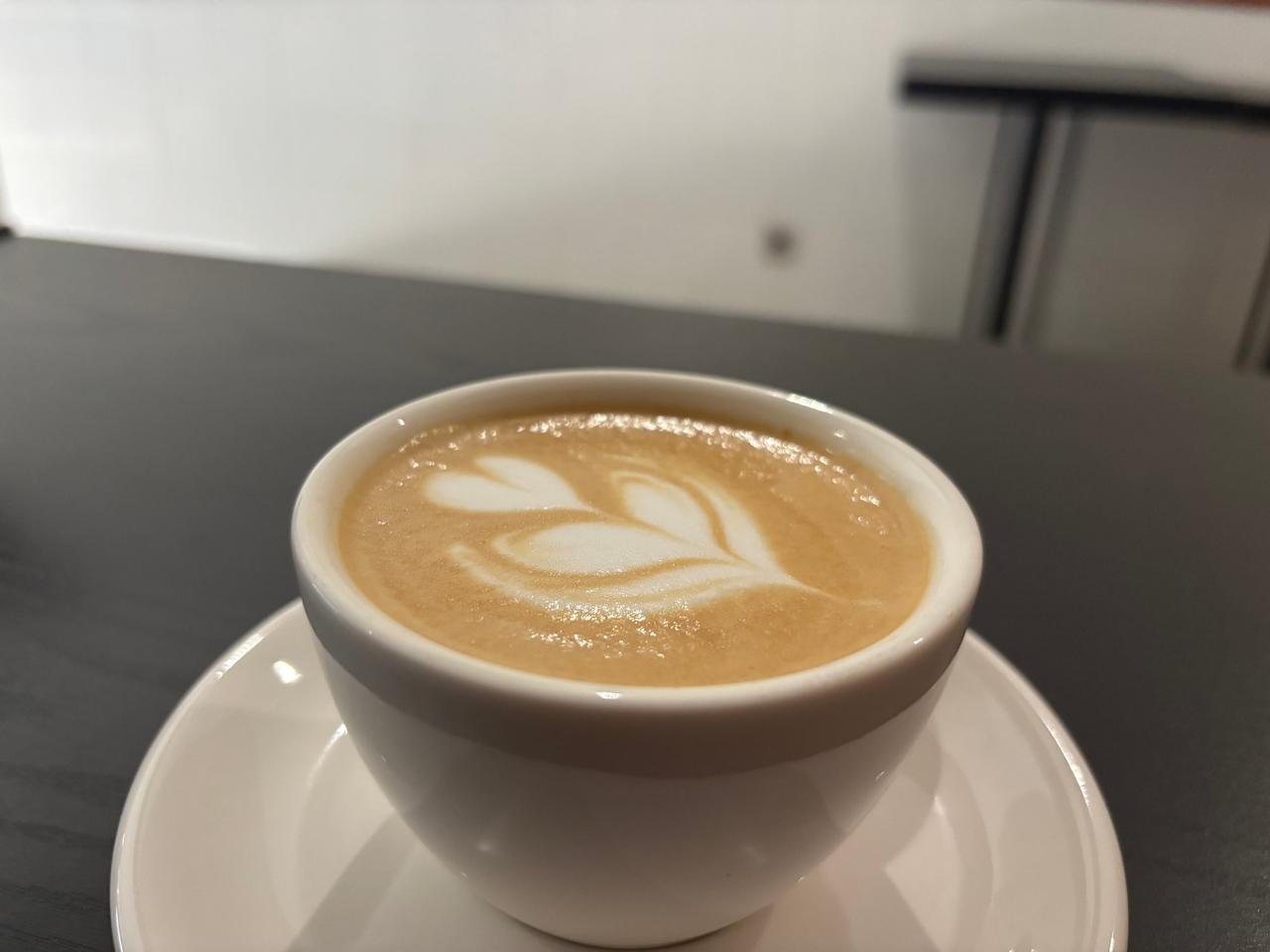 A latte with leaf-pattern latte art on a dark cafe table
