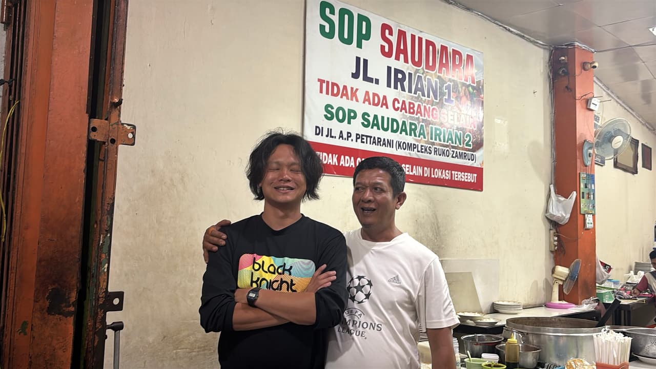 A farewell photo with an arm around the shoulder in front of a Sop Saudara restaurant sign