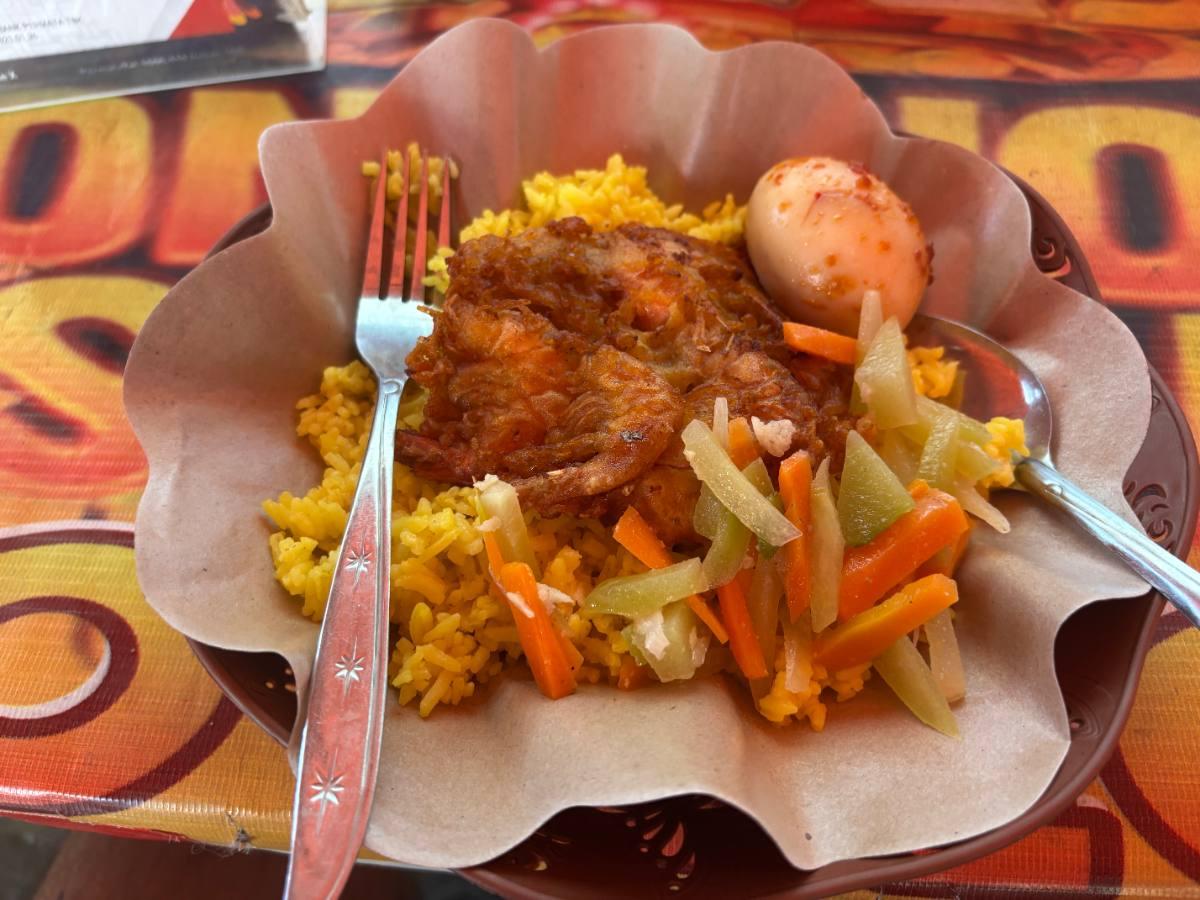 A plate of nasi kuning with fried shrimp, a boiled egg, and pickled vegetables