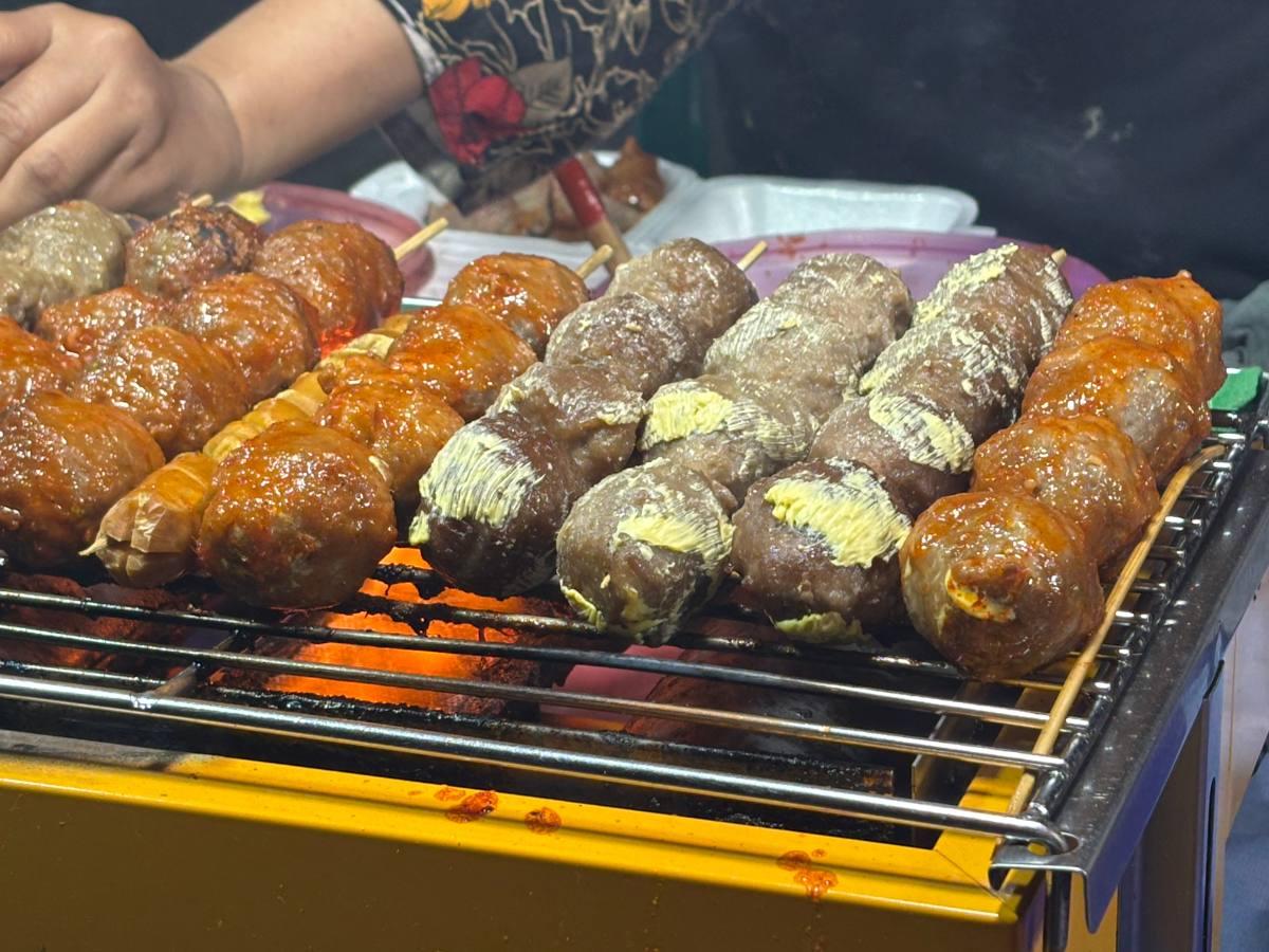 Skewers of Bakso Keju cheese-filled meatballs grilling over hot coals at a street stall