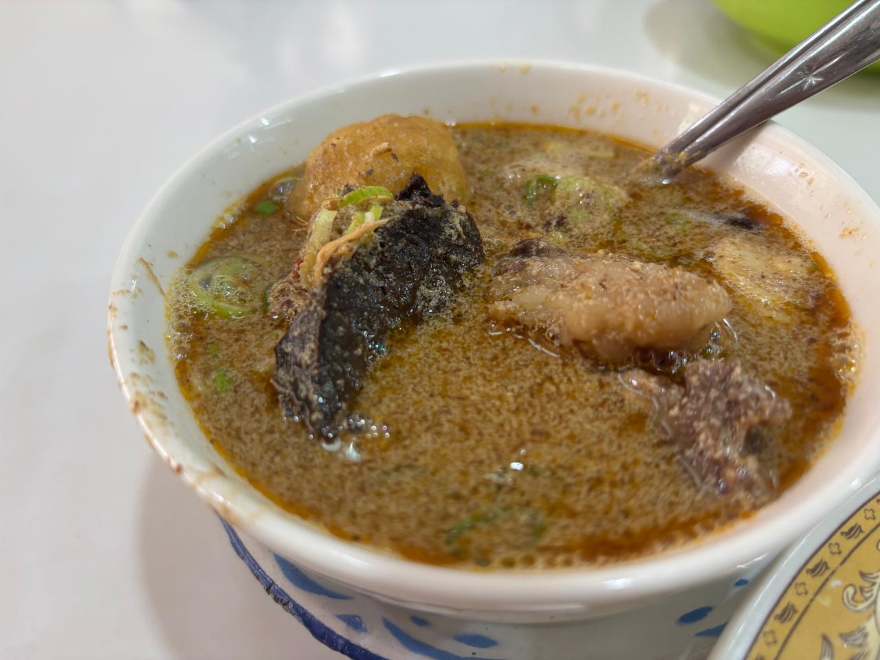 A bowl of Sop Saudara, a rich beef soup with organ meat, boiled egg and fried shallots