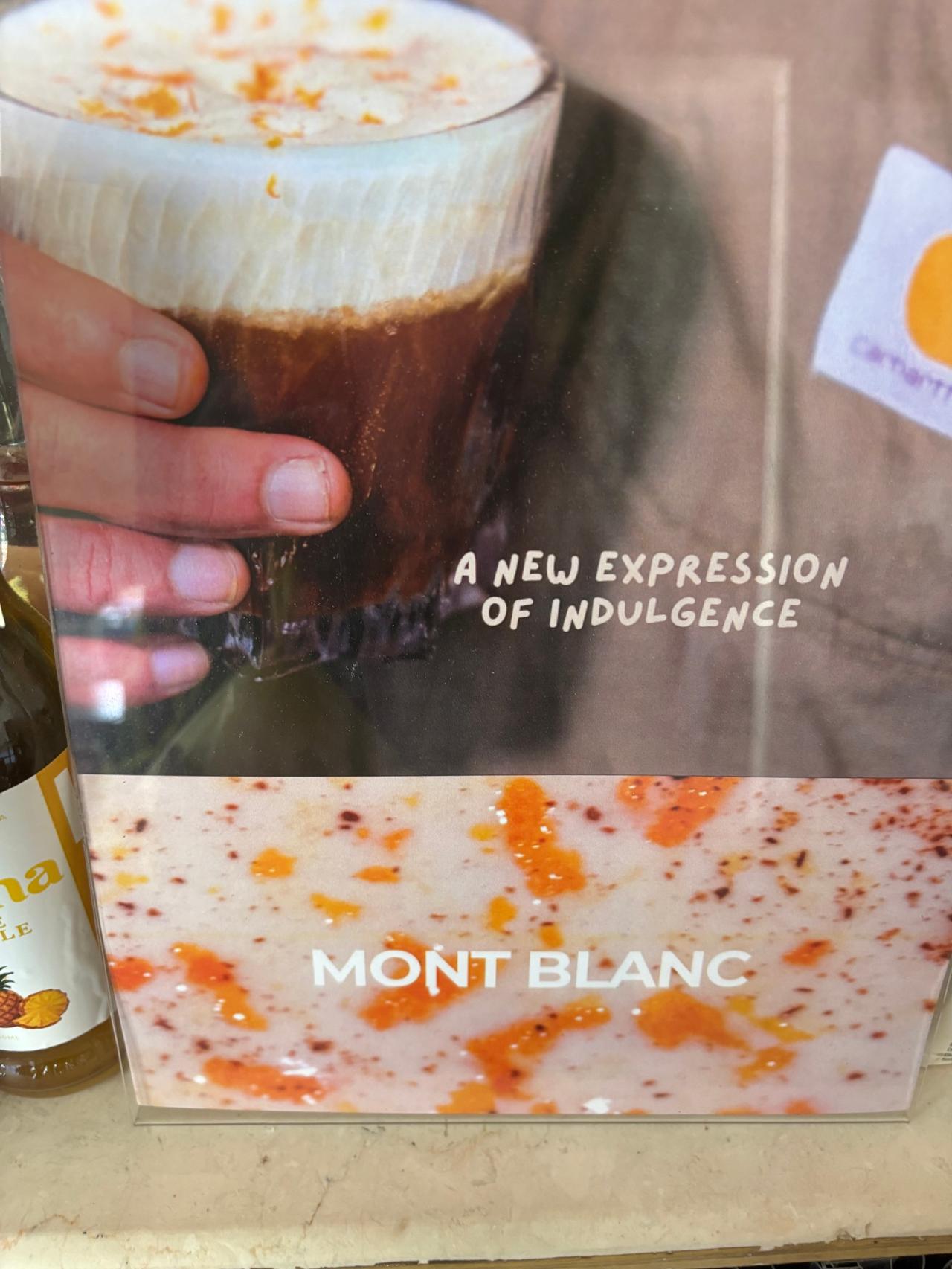 A "Mont Blanc" coffee menu sign next to a hand holding a layered iced coffee drink