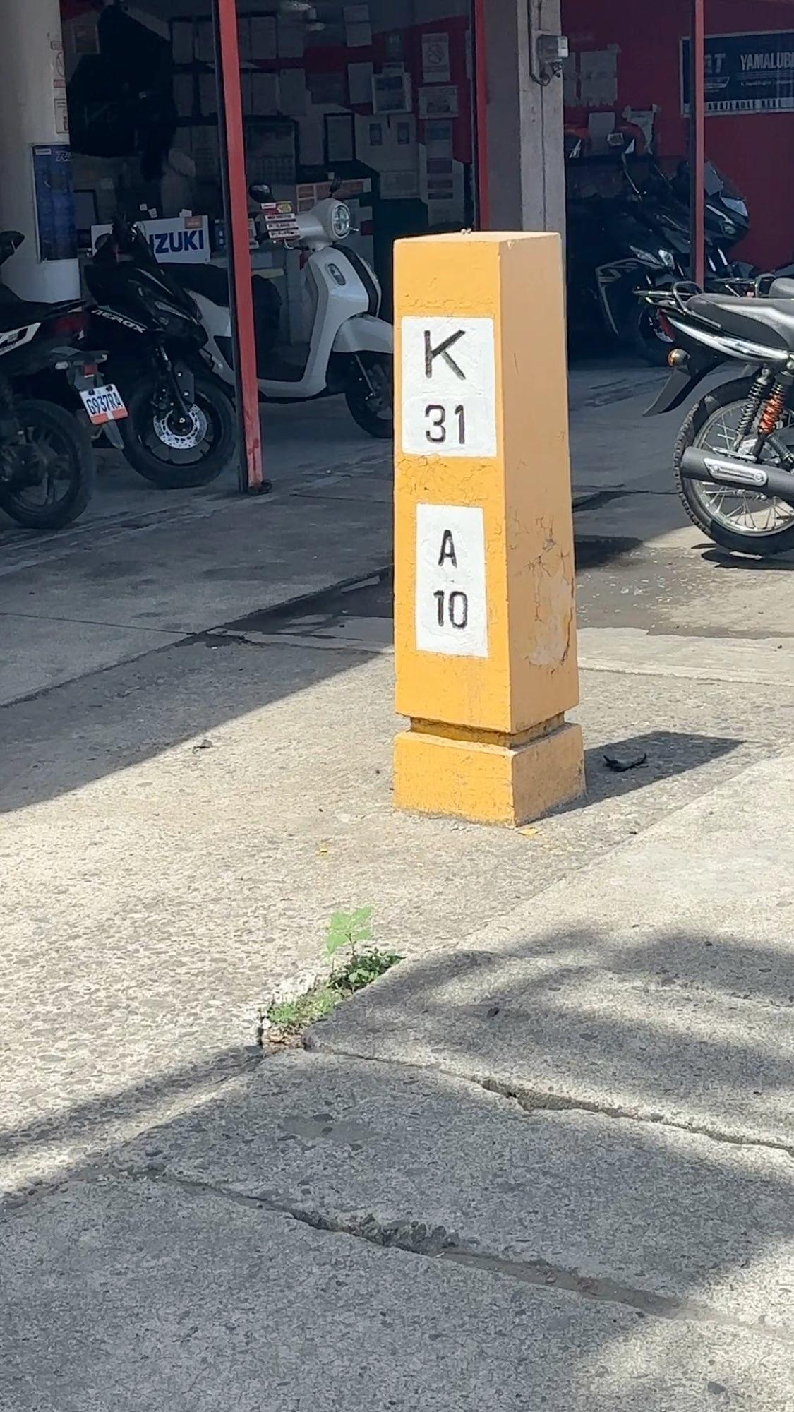 A yellow kilometer marker post on a street in Bais City, Philippines