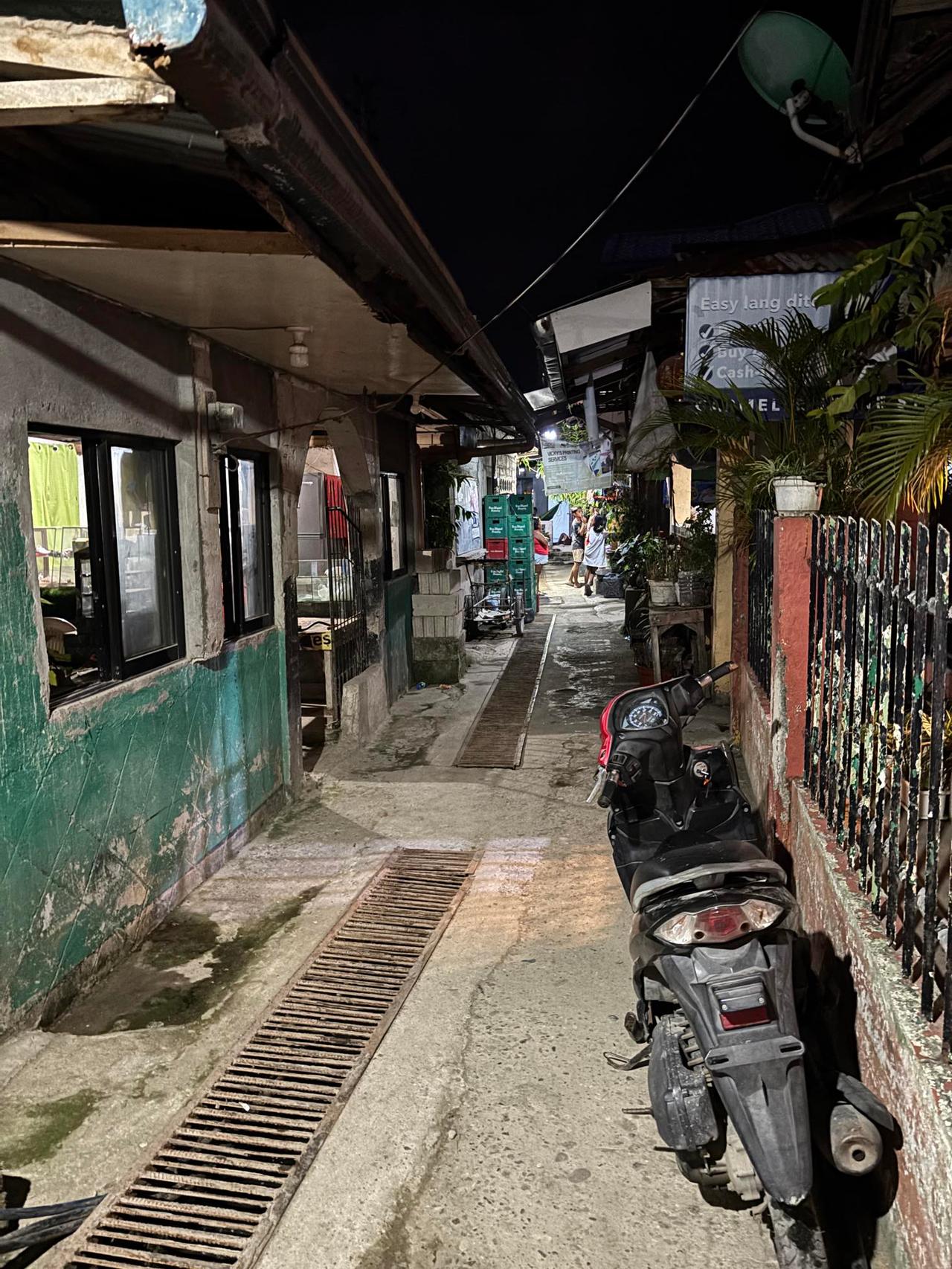 A quiet village alley at night, lit by a streetlight with a parked motorbike