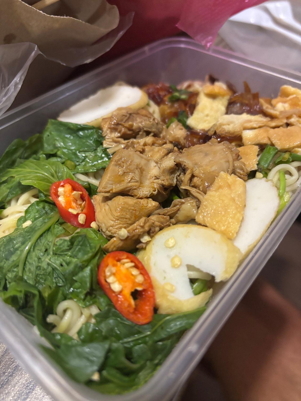 A noodle dish topped with chicken, fish cake, and fresh chili