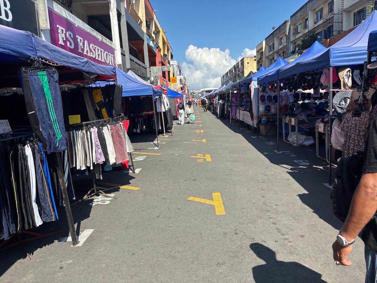 A busy clothing market street lined with vendor stalls