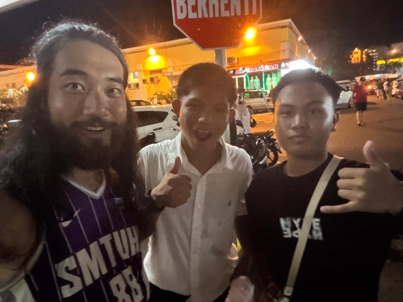 A photo with two friends under a "Berhenti" (Stop) sign at night