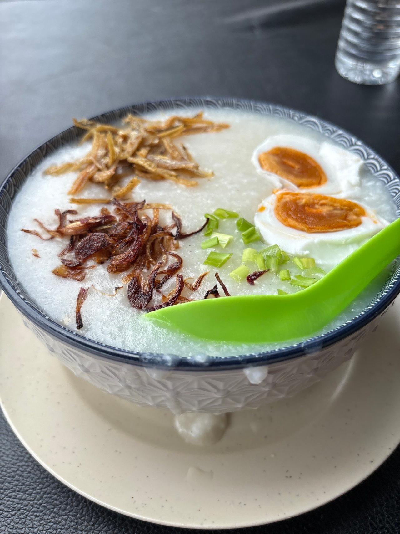 A bowl of Bubur Ayam topped with soft-boiled egg, crispy shallots, and anchovies
