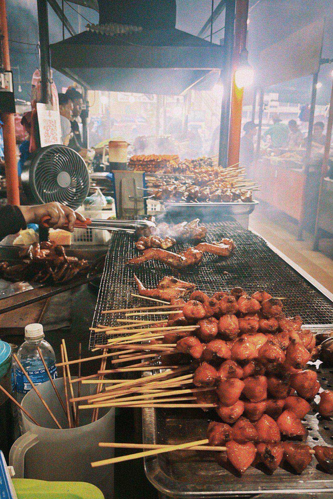 Skewered satay and grilled chicken cooking over a charcoal grill at a food stall