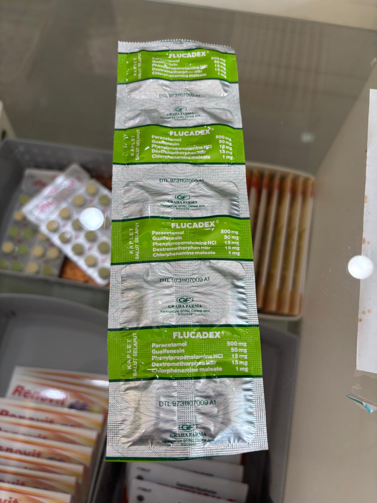 A strip of cold medicine tablets held up inside a small Indonesian pharmacy