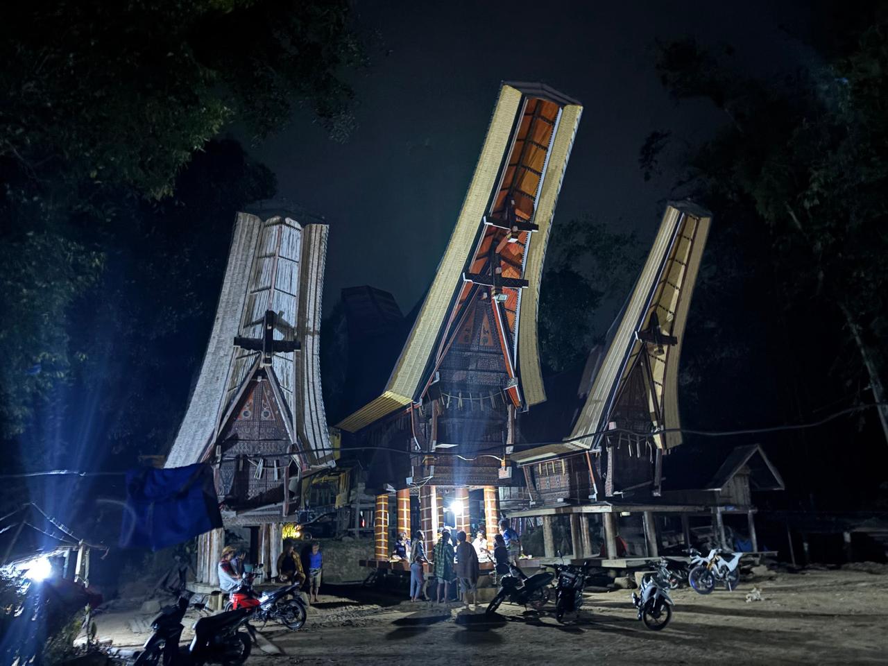 Illuminated Tongkonan houses with soaring saddleback roofs lit up against the night sky